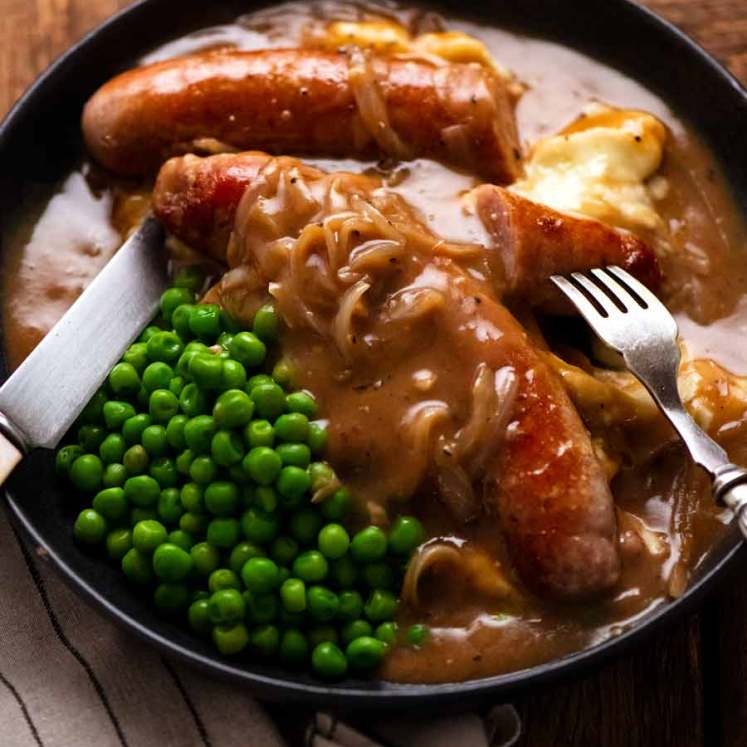 Bangers and Mash (Sausage with Onion Gravy) on a plate with mashed potato and peas