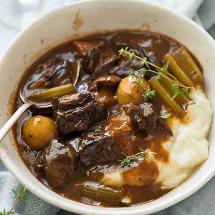Photo of Beef Stew over mashed potato in a rustic cream bowl.
